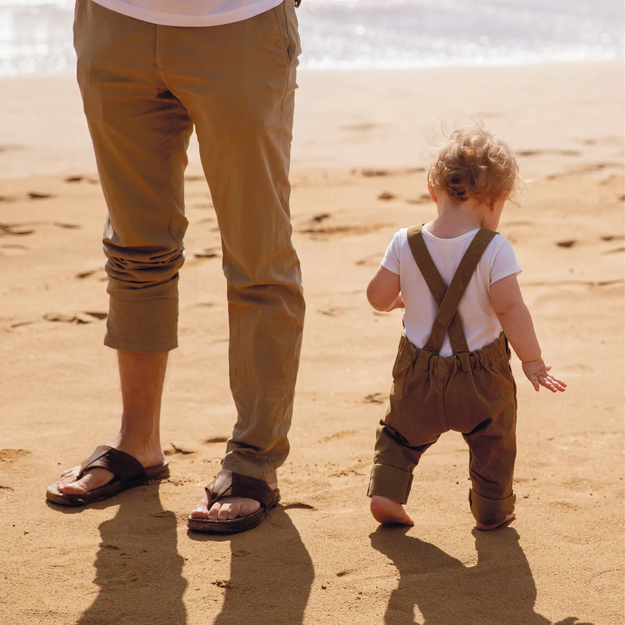 A father and his toddler walking barefoot on a beach