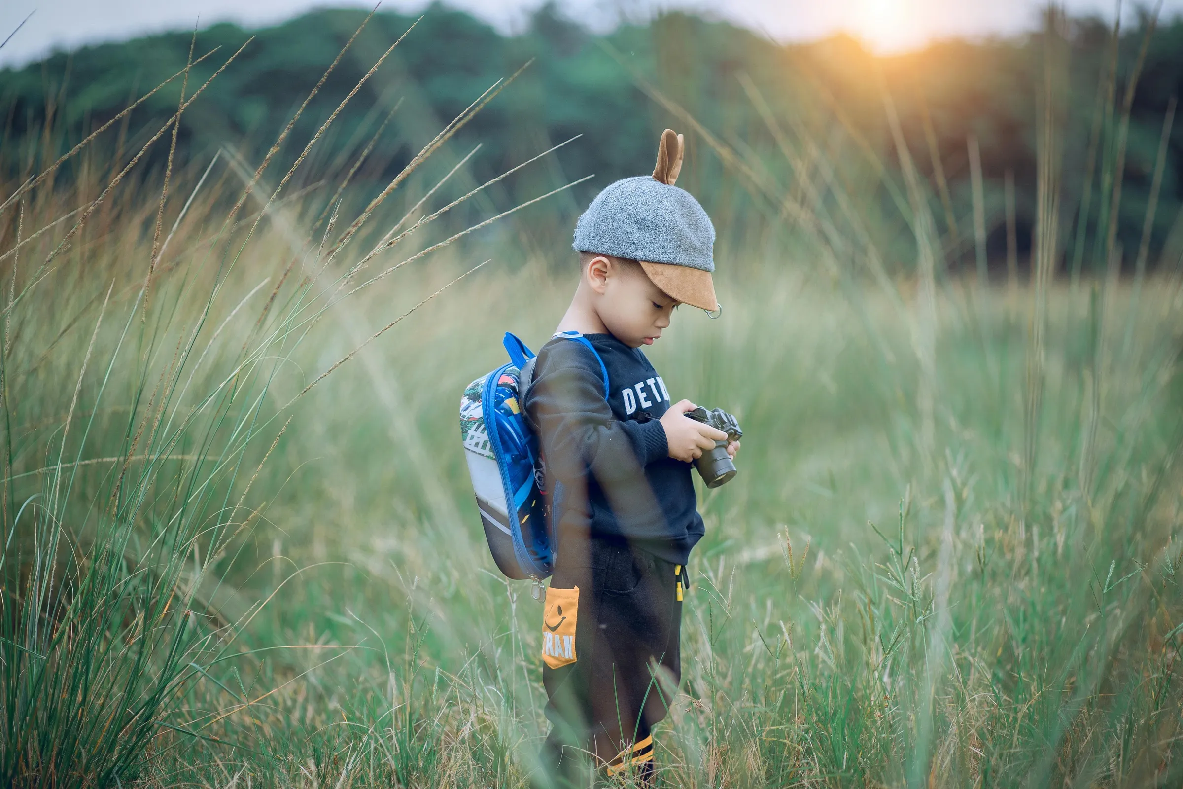 A small boy exploring tall grass with a backpack