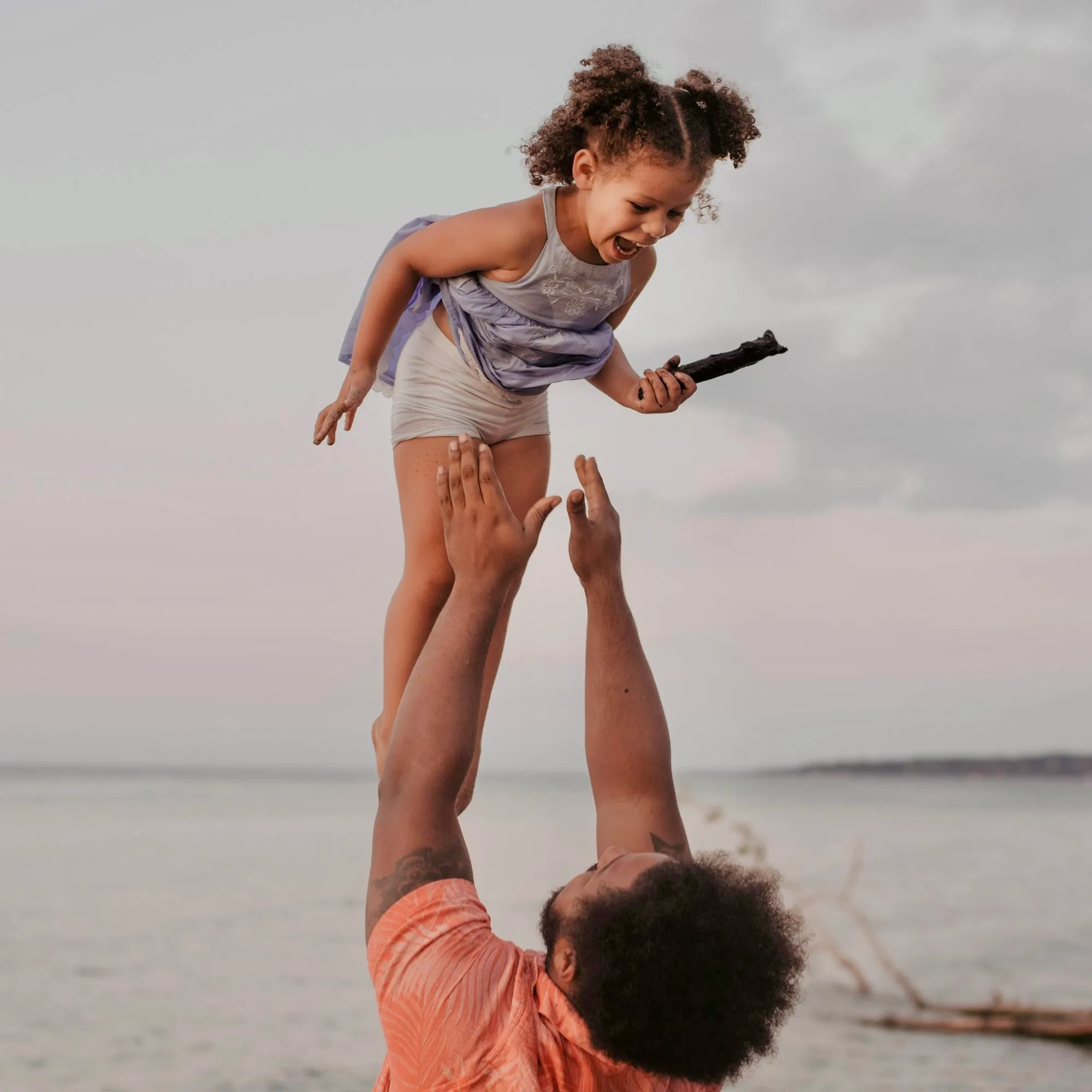 A father lifting his laughing daughter into the air by the sea