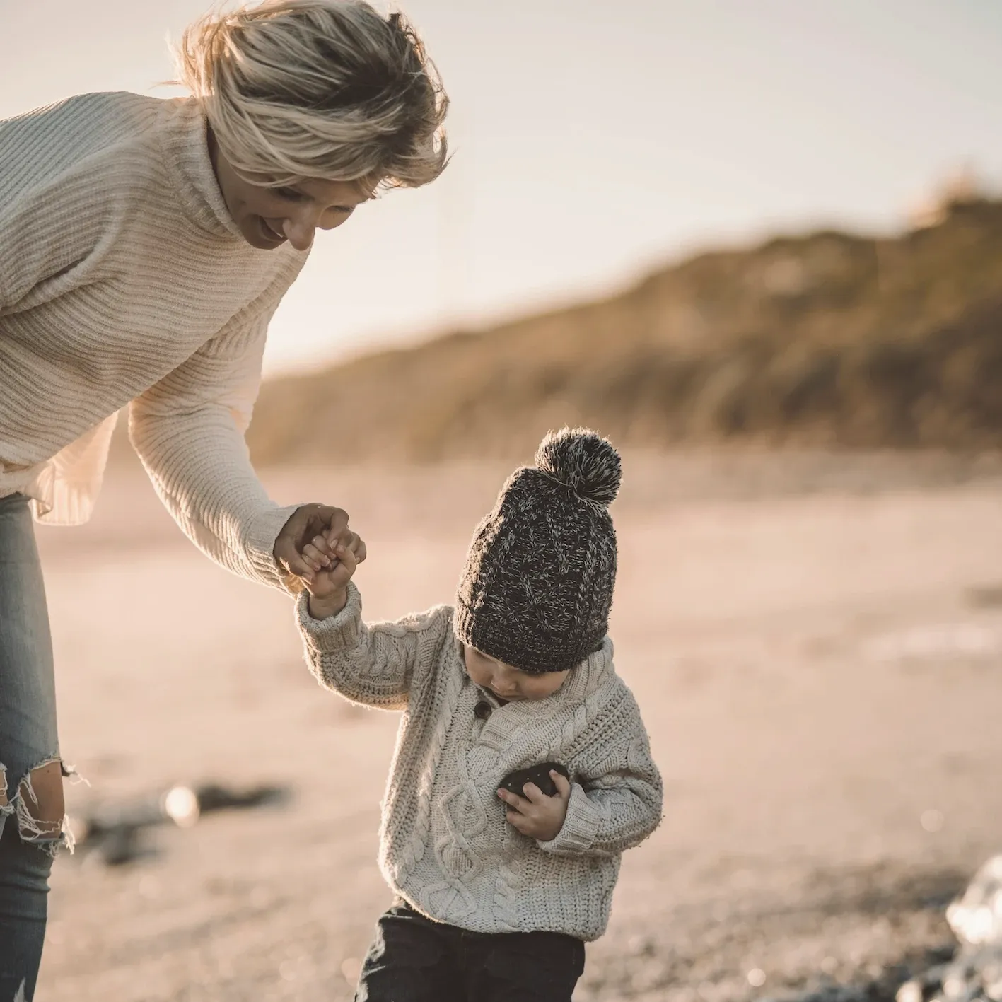 A mother holding her toddler’s hand on a beach