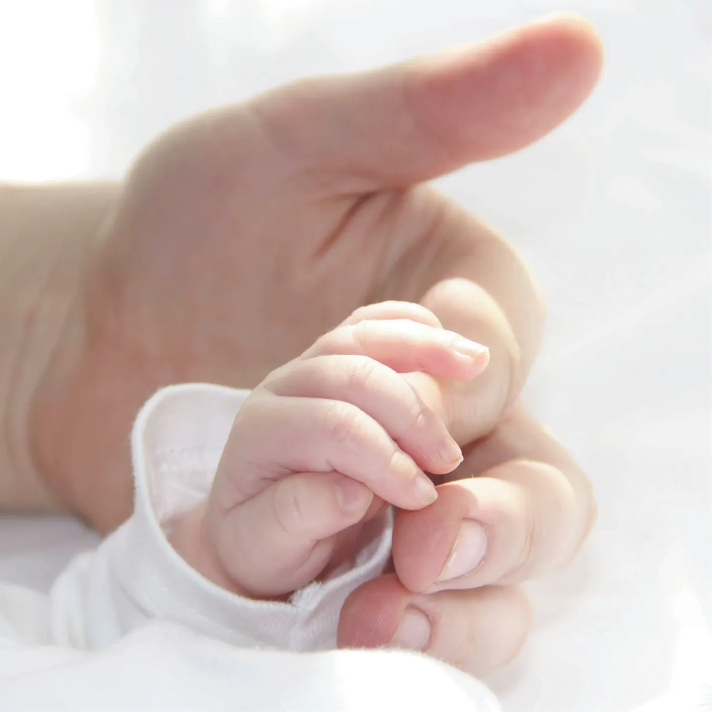 A baby’s hand holding an adult’s finger