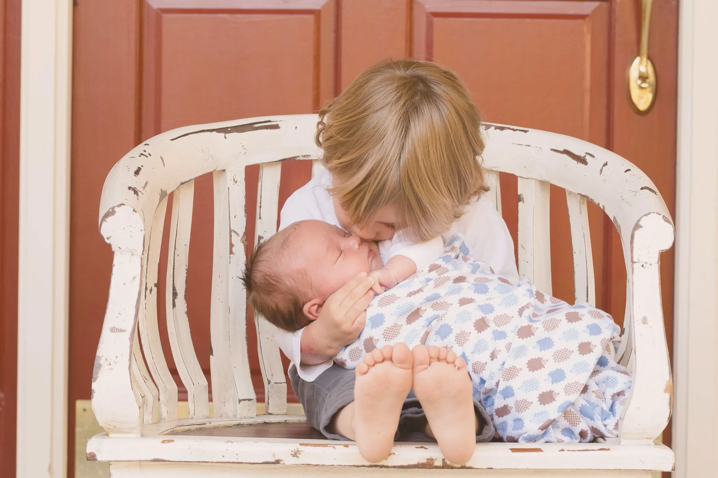 A girl kissing her baby sibling on a white bench